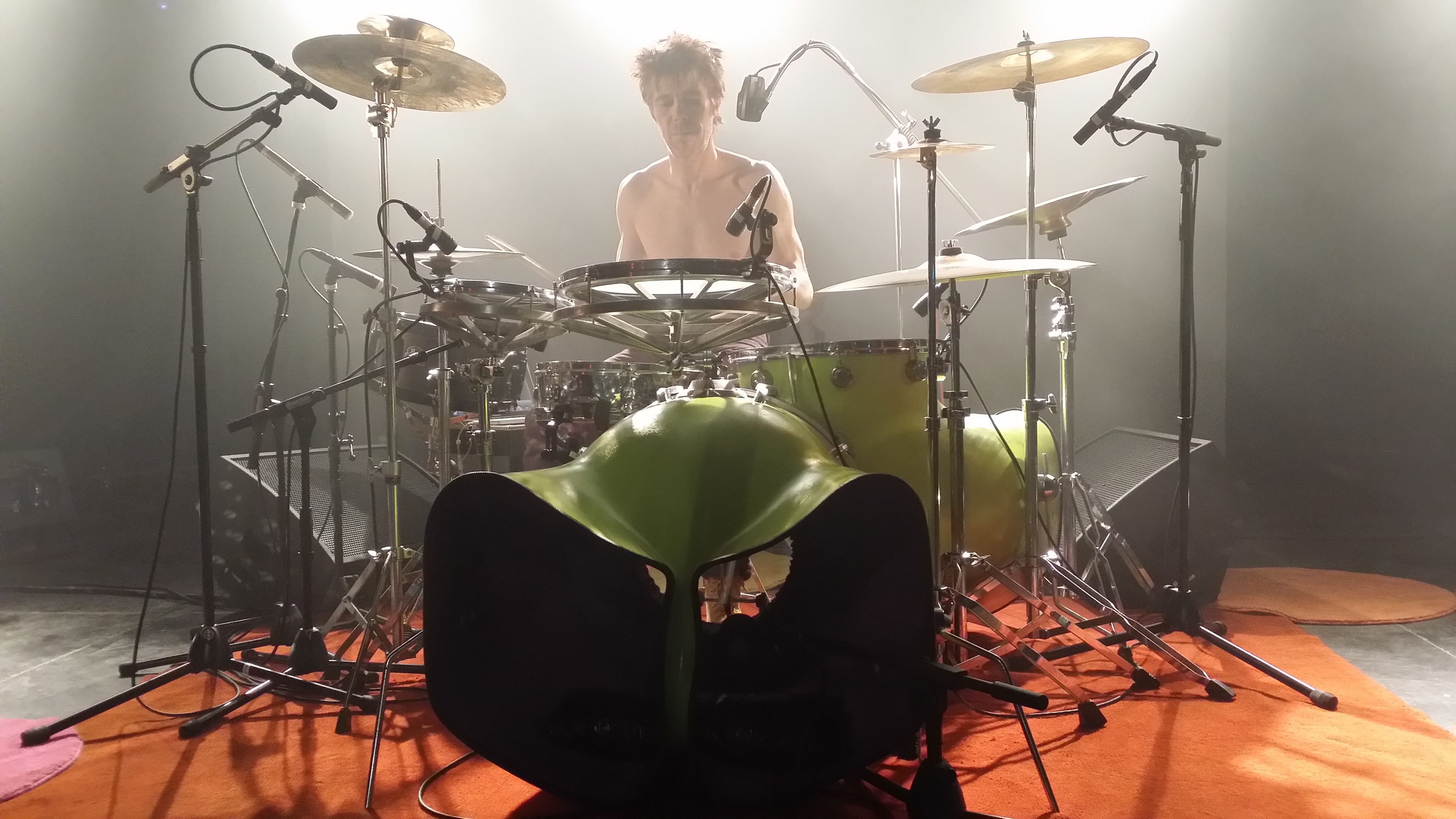 Un homme avec les cheveux rouge en pétard derrière sa batterie verte aux formes originales